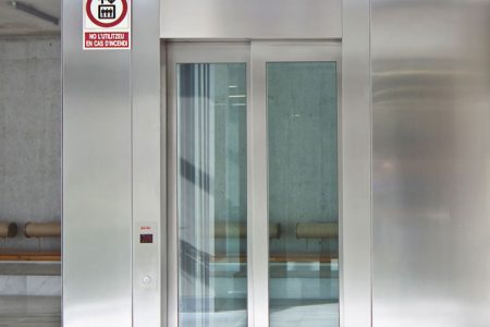Frontal de un ascensor con acabado de chapa inoxidable y puerta automática de vidrio