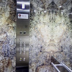 Decoración de una cabina de ascensor con bBotonera vertical de inoxidable con medio espejo y pasamano redondo