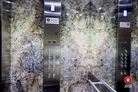 Decoración de una cabina de ascensor con bBotonera vertical de inoxidable con medio espejo y pasamano redondo
