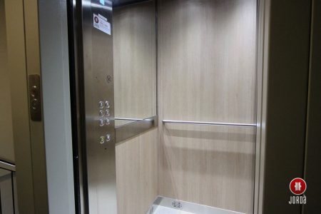 Interior de una cabina de ascensor con botonera en columna, medio espejo y paredes de formica