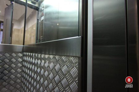 Interior de una cabina de ascensor con pared de chapa estriada y medio espejo